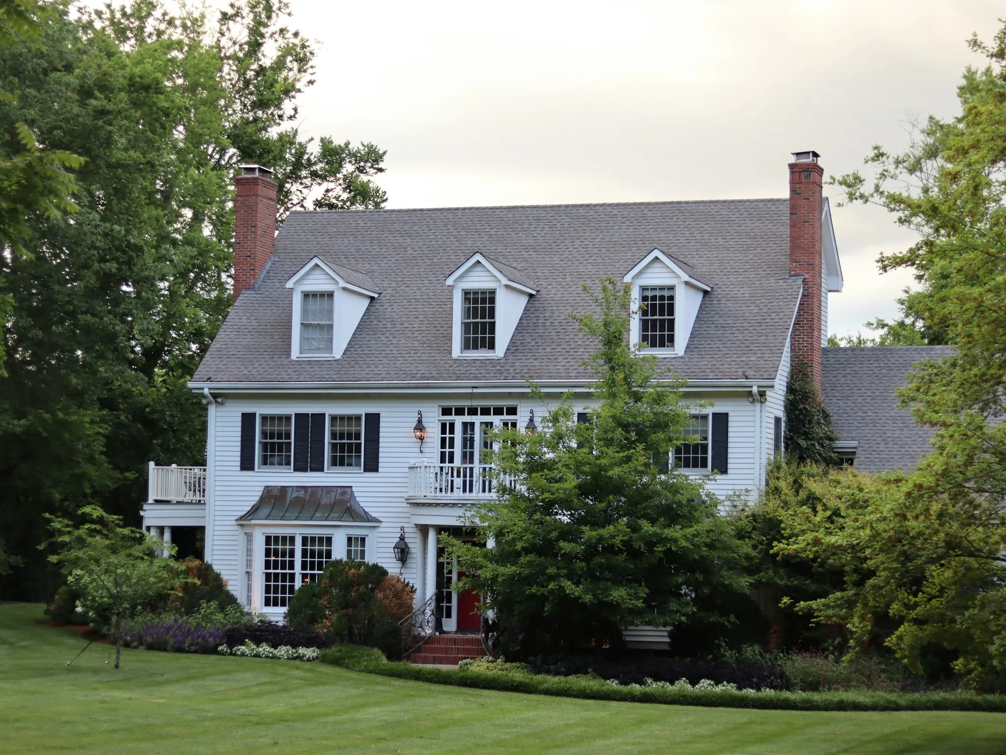 Two-story white colonial home with dormers and a landscaped front yard
